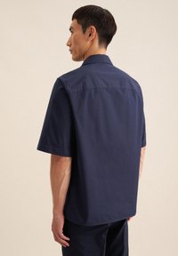 Korte mouwen donkerblauw shirt, met kraag en een gladde textuur, voorzien van een rugpanddetail en een rechte zoom. Draag met bijpassende donkerblauwe broek.