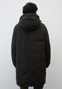 Zwarte lange pufferjas met capuchon, met een gladde textuur en een minimalistisch ontwerp, gezien van achteren tegen een neutrale achtergrond.
