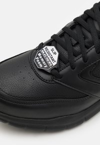 Zapatillas negras antideslizantes hechas de cuero texturizado con plantilla de espuma con memoria. Cuenta con cordones negros y un detalle en forma de hexágono.