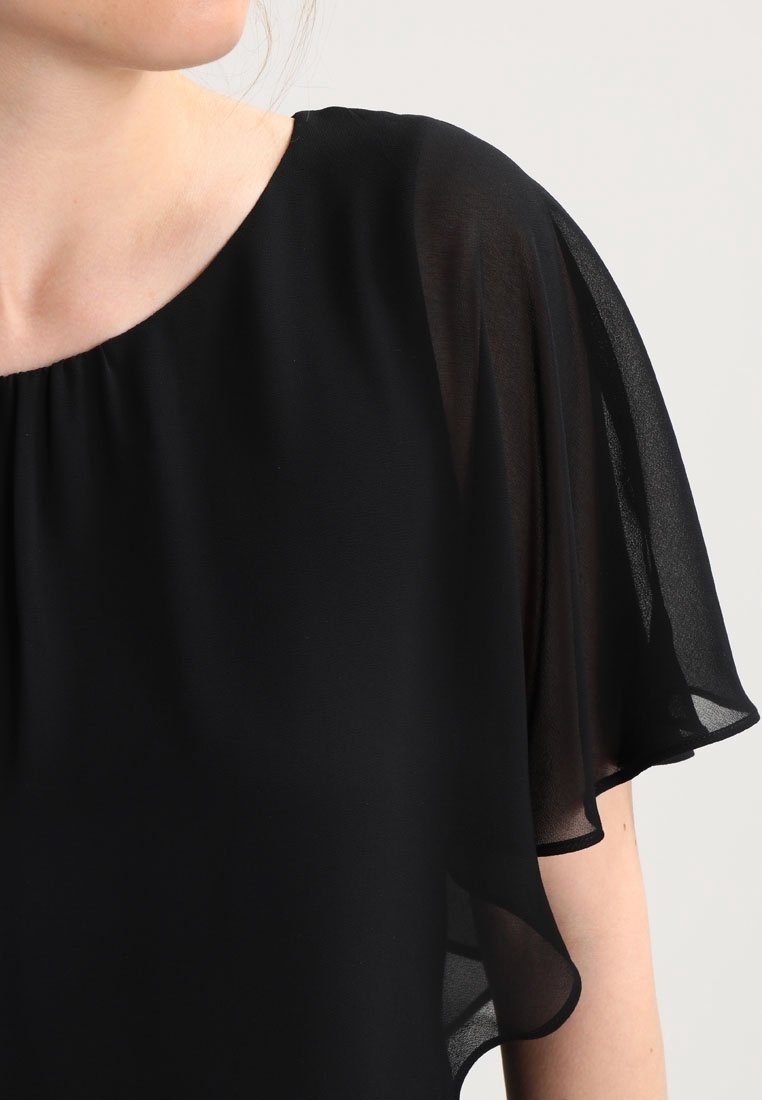Zwarte blouse met losse, doorzichtige korte mouwen. Het materiaal is lichtgewicht en vloeiend, met een ronde halslijn en subtiele draping.