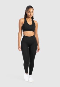 Zwarte sport-bh met een ronde hals en racerback, gecombineerd met hoge zwarte leggings. Soepele textuur, aansluitend ontwerp en witte sneakers.