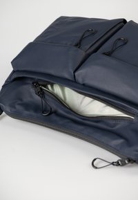 Marineblauwe rugzak met twee voorvakken, een centraal ritsvak met een zwarte rits en een gladde, gestructureerde buitenkant.