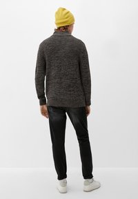 Grå strukturerad stickad tröja, svarta jeans, vita sneakers och en gul mössa. Bakåtsikt visar tröjans krage och vävda mönster.