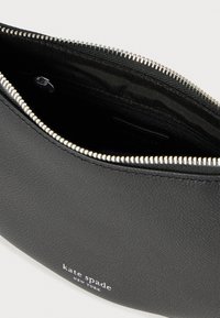 Fekete bőr erszény texturált felülettel, ezüst cipzárral és bélés belsővel, amelyen a márka logója fehérrel van nyomtatva.