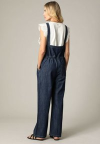 Denim tuinbroeken met wijde pijpen, een getailleerde taille en een fitted wit top met gekartelde kant mouwen. Donkerblauwe stof met zakken.