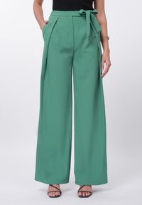 Zelene široke hlače iz gladkega blaga z zavezanim pasom, gubami spredaj in stranskimi žepi.
