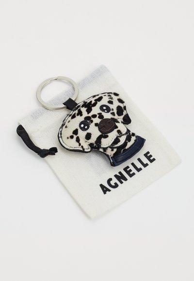 Porte-clés en forme de dalmatien en matériau texturé noir et blanc, avec des détails pour les yeux et le nez. Accompagné d'une pochette en tissu blanc étiquetée "AGNELLE."