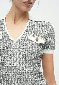 Haut en tricot texturé gris et blanc avec un col en V, des manches courtes, un col blanc et des accents de métal doré sur les poches.