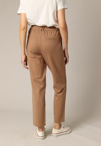 Pantalons marron ajustés avec une taille élastique, dotés de deux poches arrière, associés à des baskets blanches et une chemise blanche ample.
