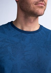 Blauwe katoenen T-shirt met een gestructureerd patroon, voorzien van een ronde hals en korte mouwen. Het ontwerp bevat subtiele loofvormen in een donkere tint.