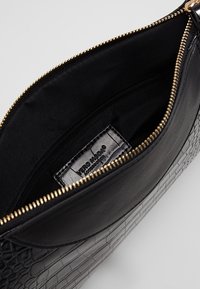 Sac en cuir synthétique noir avec un motif crocodile texturé, une fermeture éclair dorée et une doublure en tissu noir avec une poche intérieure zippée.