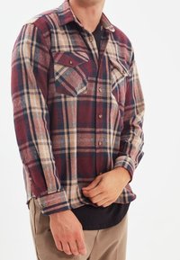 Camicia di flanella a quadri rossi e beige con due tasche sul petto, chiusura frontale con bottoni e maniche lunghe. Texture morbida, design casual.