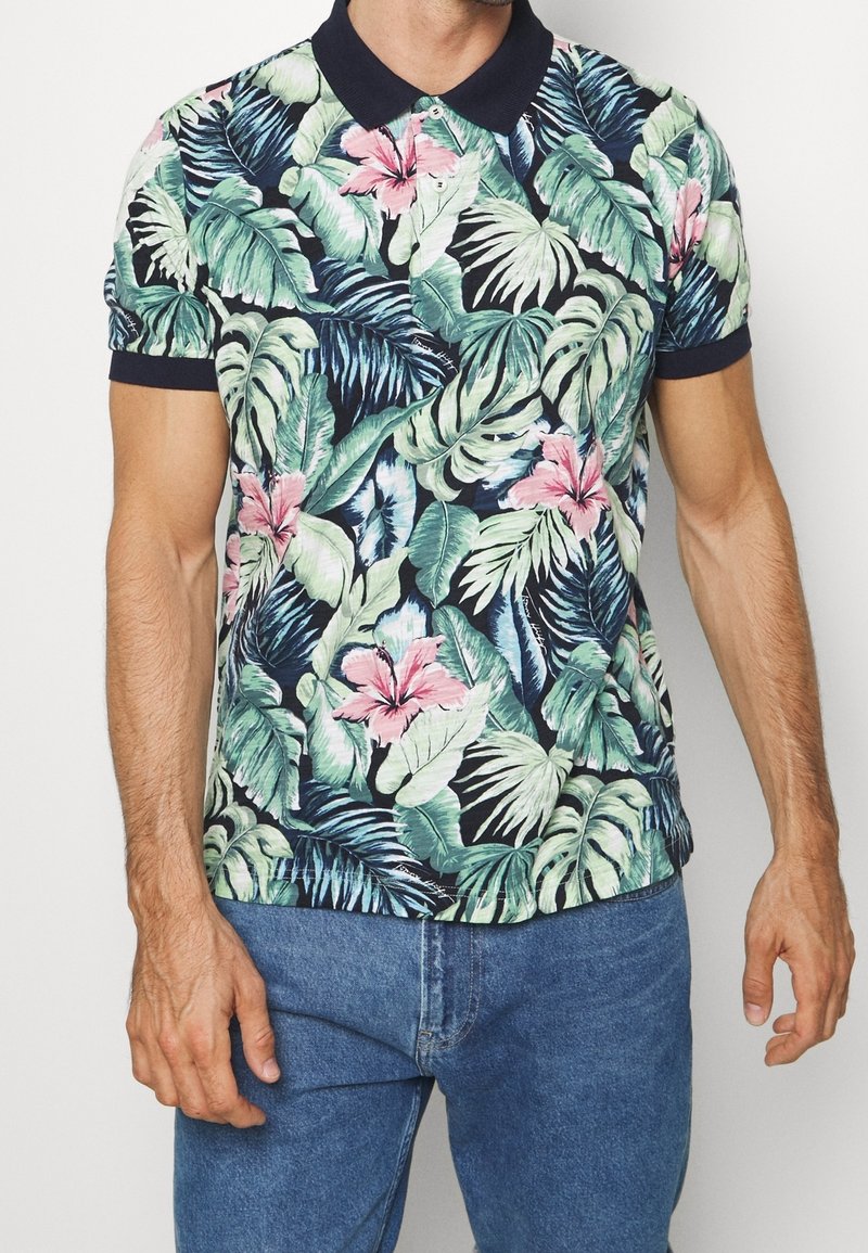 Koszulka polo z krótkim rękawem, ozdobiona tropikalnym wzorem liści i kwiatów w zielonym, różowym i granatowym kolorze, z jednolitym granatowym kołnierzykiem i mankietami rękawów.