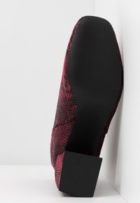 Chaussure à talon haut motif serpent rouge avec une tige texturée et une semelle en caoutchouc noire. Le talon est carré et robuste, offrant une meilleure stabilité.