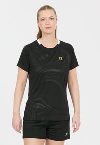 Svart atletisk skjorta med korta ärmar, med ett texturerat vågmönster och en vit krage. Logotypen "FZ" i guld på vänster bröst.