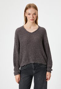 Grijze, gemêleerde gebreide sweater met een V-hals, ruime pasvorm en lange mouwen. Gecombineerd met donkere jeans met een subtiel ribbelpatroon.