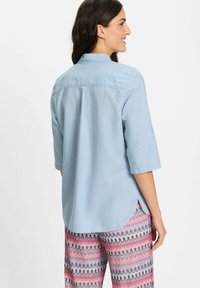 Light blue button-up shirt with a standing collar, short sleeves, and back pleat detail, paired with patterned multi-colored pants.