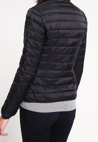 Black puffer jacket with a quilted design, high collar, and zip closure. Features long sleeves and a fitted waist, made of glossy material.