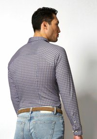 Langarmhemd in Marineblau mit weißem geometrischen Muster, ausgestattet mit einem Kragen und knöpfbaren Manschetten, kombiniert mit hellblauen Jeans und einem braunen Gürtel.