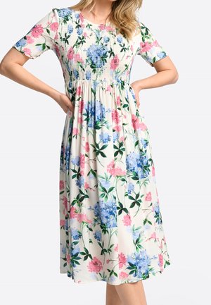 Robe florale avec des manches courtes, un corsage smocké et une jupe fluide. Les couleurs incluent des fleurs roses et bleues sur un fond crème.