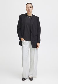 Černý blazer se dvěma knoflíky, kombinovaný s černým tričkem a bílými kalhotami širokého střihu. Vyznačuje se minimalistickým designem a texturovanou látkou.