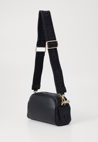 Svart läder crossbody-väska med strukturerad yta, guld detaljer och en rem med ett märkesleder svart tygaccent. Dragkedjestängning.