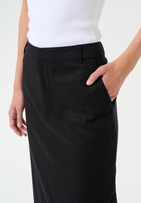 Fustă neagră cu o textură netedă, prevăzută cu buzunare laterale și o croială ajustată. Talia este plată, oferind o siluetă curată.