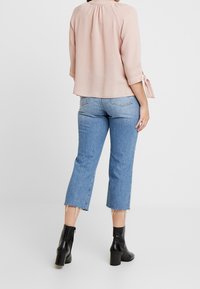 Blusa leggera rosa chiaro e fluida con maniche a tre quarti, pieghe sul retro, abbinata a jeans cropped blu chiaro e stivaletti neri con tacco.