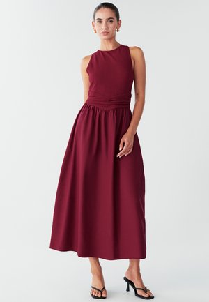 Burgundy-maximekkoin, jossa on tiukka yläosa, ribbattu pinta ja kootut vyötärö, jossa on sileä hame ja minimaliset hihnat.
