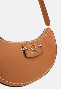 Sac à bandoulière en cuir marron avec une forme arrondie. Il comporte un rabat avec un logo argenté et une couture contrastante le long du bord. Fermeture éclair en haut.