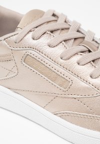 Närbild av en ljusbeige lädersneaker med tonala snören, detaljerad sömnad och en strukturerad vit gummisula.