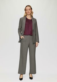 Grau maßgeschneiderter Anzug mit einem strukturierten Blazer und weiten Hosen, kombiniert mit einer dunkelburgunderfarbenen Bluse. Schwarze spitze Pumps runden das Outfit ab.