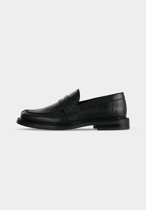Mocasín penny negro de cuero para hombre con tacón bajo y apilado y puntera redondeada, mostrado de lado sobre un fondo gris claro.