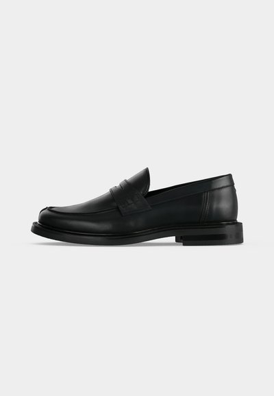 Mocassin penny pour homme en cuir noir avec talon bas empilé et bout arrondi, vu de profil sur fond gris clair.