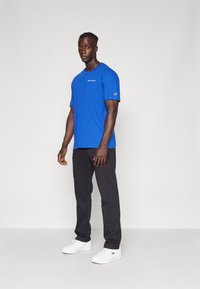 T-shirt en coton bleu avec un col rond, arborant un petit logo blanc sur la poitrine. Associé à un pantalon noir et des baskets blanches.