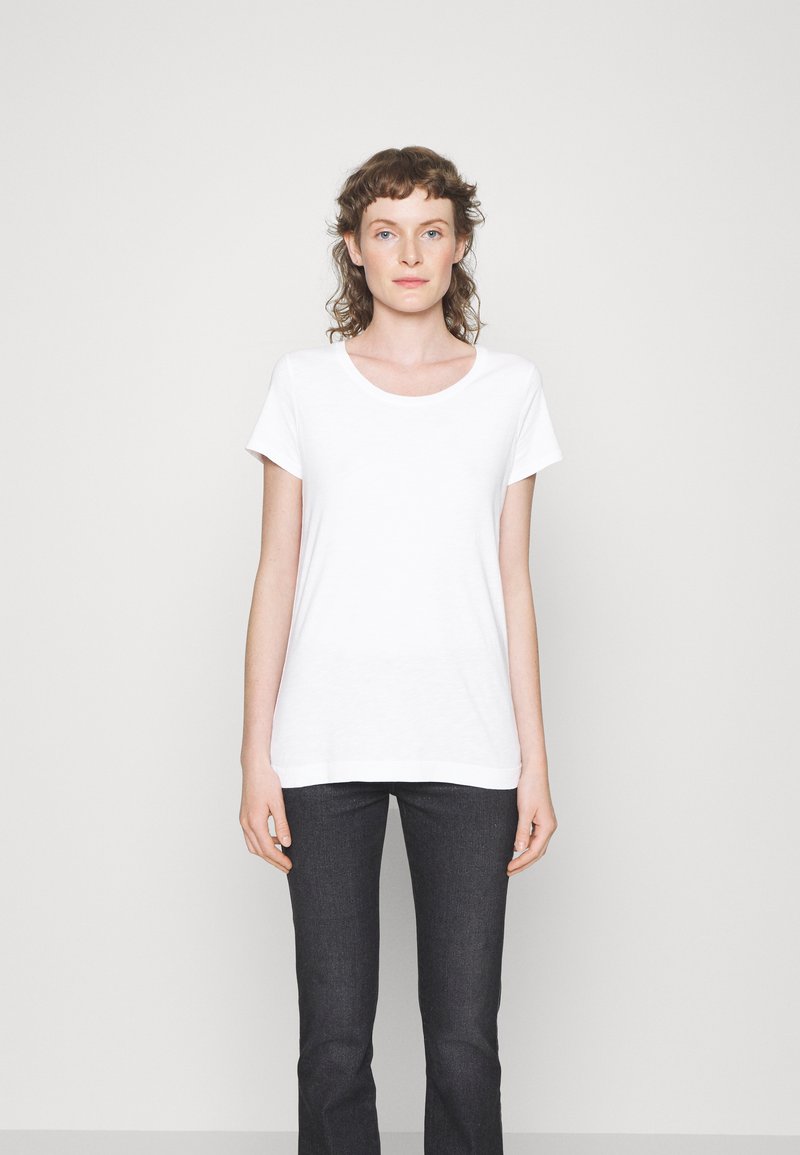 Weißes T-Shirt mit kurzen Ärmeln und rundem Halsausschnitt, aus leichtem Stoff, kombiniert mit dunklen Jeans. Einfaches und grundlegendes Design.