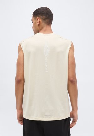 Čovjek u bezrubljoj bež majici s natpisom "Never Stop Moving" i grafikom na leđima, uparenom s crnim hlačama.