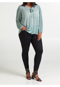Blusa verde menta con pois, con bottoni sul davanti e fiocco al collo, abbinata a jeans skinny neri e sandali neri con borchie.