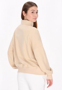 Ljusbeige pullover i mjukt tyg, med hög krage, lös passform, sänkt axlar samt ribbade muddar och nederkant.