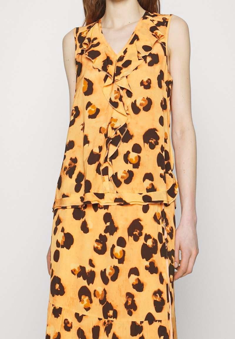 Blouse jaune sans manches à imprimé léopard marron, col en V à volants et jupe assortie portée par une personne cadrée aux épaules et aux hanches.