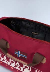 Borsa di tessuto bordeaux con interno nero, chiusura con zip, manici marroni e una toppa con la bandiera dell'Islanda. Presenta un'etichetta del marchio all'interno.