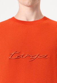 Maglione arancione lavorato a maglia con un motivo a coste testurizzato e scollo rotondo. Presenta il logo ricamato "Tanga" in una tonalità di arancione più chiara.