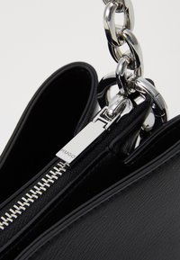 Zwart leren handtas met zilveren kettinghengsel en ritssluiting. De rits heeft een gemarkeerde trekker en toont een gladde textuur en strak design.