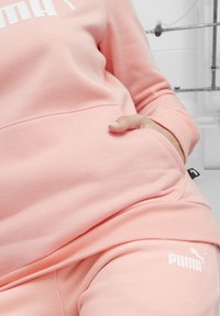Felpa rosa e pantaloni jogger realizzati in tessuto morbido, con tasca a marsupio e logo Puma bianco. Polsini a coste con una finitura testurizzata.