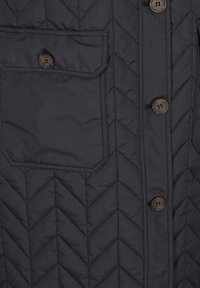 Gilet matelassé noir avec un motif en chevron, fermeture à boutons sur le devant et une poche poitrine avec un détail de bouton. Texture douce et matériau durable.