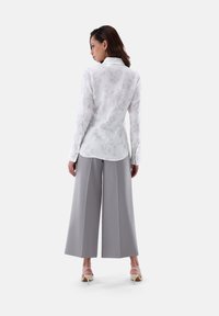 Camicia bianca con bottoni e stampa floreale, abbinata a pantaloni larghi grigi chiari e décolleté nudi. Tessuto morbido, vestibilità su misura.