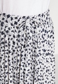 Jupe plissée bleu marine et blanche avec un motif floral, dotée d'une taille à cordon de serrage et d'une texture de tissu léger.