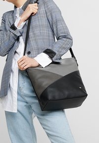 Bolso de cuero negro y gris con diseño angular, superficies texturizadas y una correa de hombro negra. Patrones triangulares distintivos en los lados.