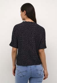 Blusa nera a maniche corte con pois bianchi, presenta un collo rotondo e delicate rifiniture arricciate lungo i bordi.