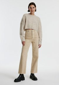 Beige cropped gebreid trui gecombineerd met beige high-waisted wijde broek. Zwarte chunky enkelboots maken de outfit compleet. Zachte textuur, relaxte pasvorm.